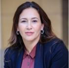 A person with long hair wearing a dark blue jacket and burgundy shirt
Description automatically generated